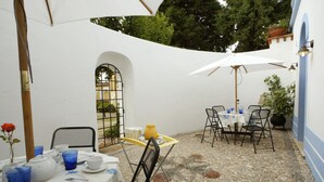 Une terrasse extérieure avec des tables disposées pour les repas, entourée de murs blancs et dotée d’un sol en pierre.