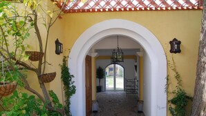 Une entrée en arc surmontée de jardinières suspendues et un chemin menant à une porte.