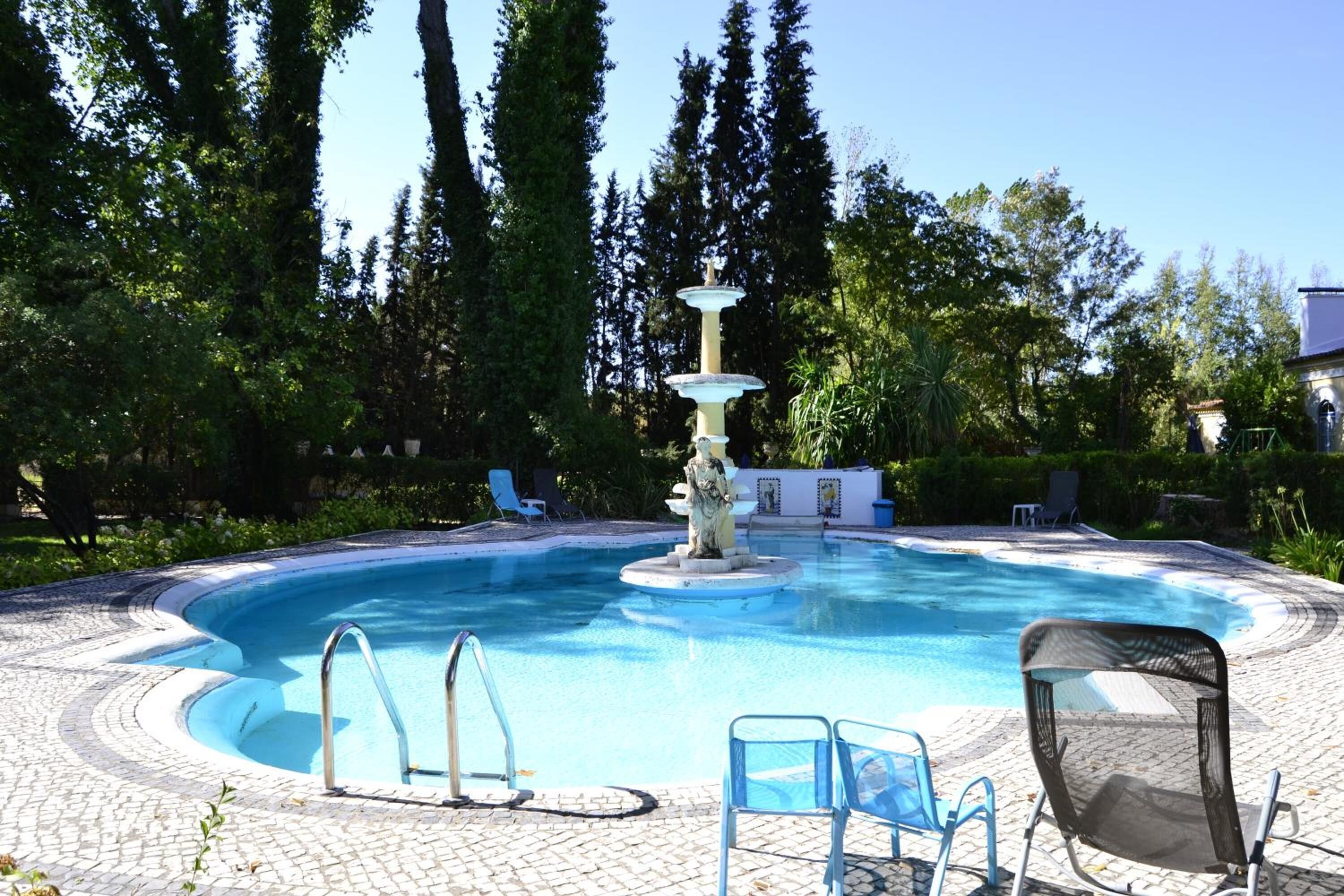 A swimming pool with a fountain, surrounded by lounge chairs and a paved deck.