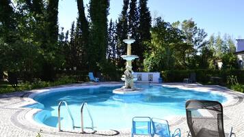Piscina com uma fonte, cercada por espreguiçadeiras e um deck pavimentado.