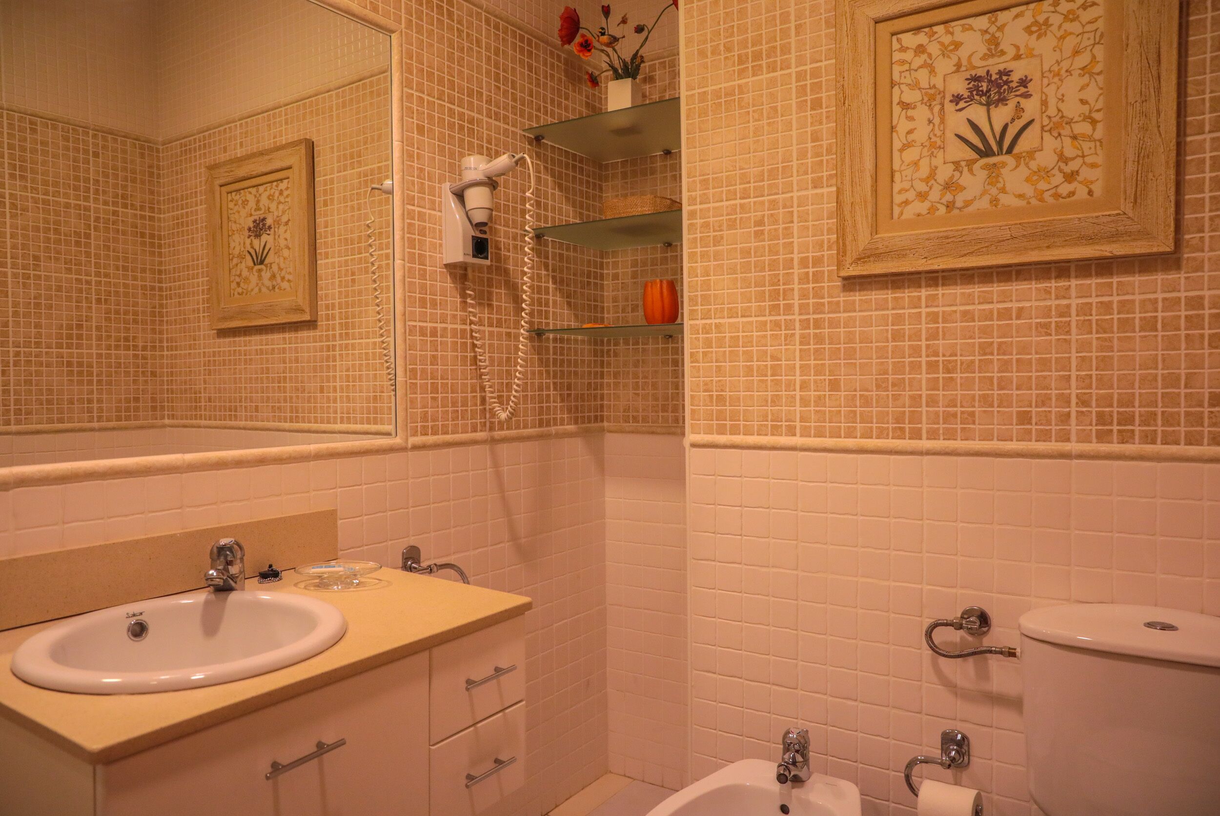 Une salle de bain équipée d’un lavabo, d’un miroir, de toilettes et d’étagères contenant des articles de toilette.