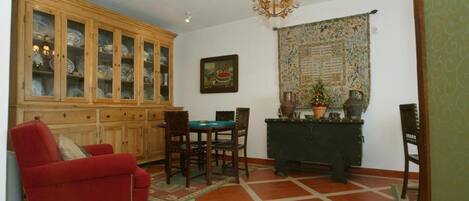 A living room with a red sofa, wooden cabinet with glass doors, a dining table with chairs, a chandelier, and a tapestry on the wall.