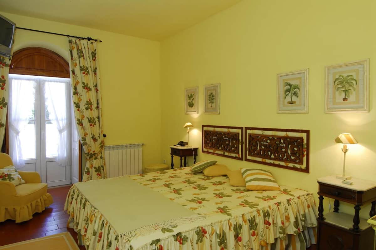 Ein Schlafzimmer mit einem Bett, einem Sessel, einem Nachttisch, einer Lampe und einer Tür mit Vorhängen.