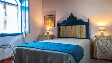 A bedroom with a bed, a window, a bedside table, a lamp, and a framed picture on the wall.