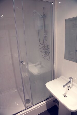 A glass-enclosed shower with a handheld showerhead and a wall-mounted faucet.