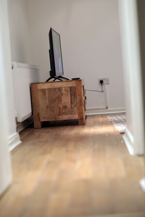 A wooden cabinet with a television on top, a power outlet on the wall, and a radiator in the background.