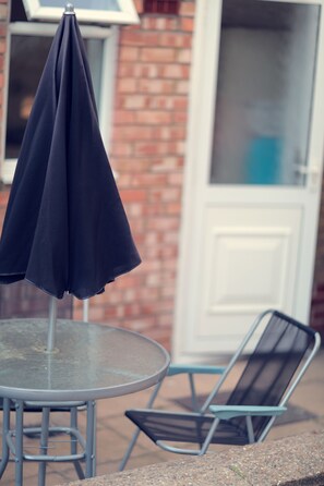 A round metal table with a glass top, a blue umbrella, and a black metal chair.
