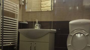A bathroom with a toilet, sink, mirror, towel rack, and a shower area.
