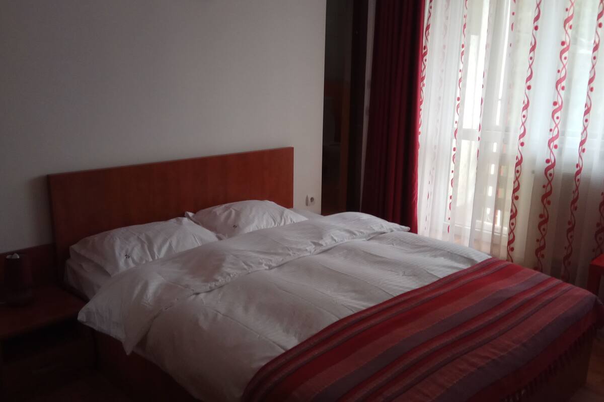 A hotel room with a bed, a nightstand, and a red bench.