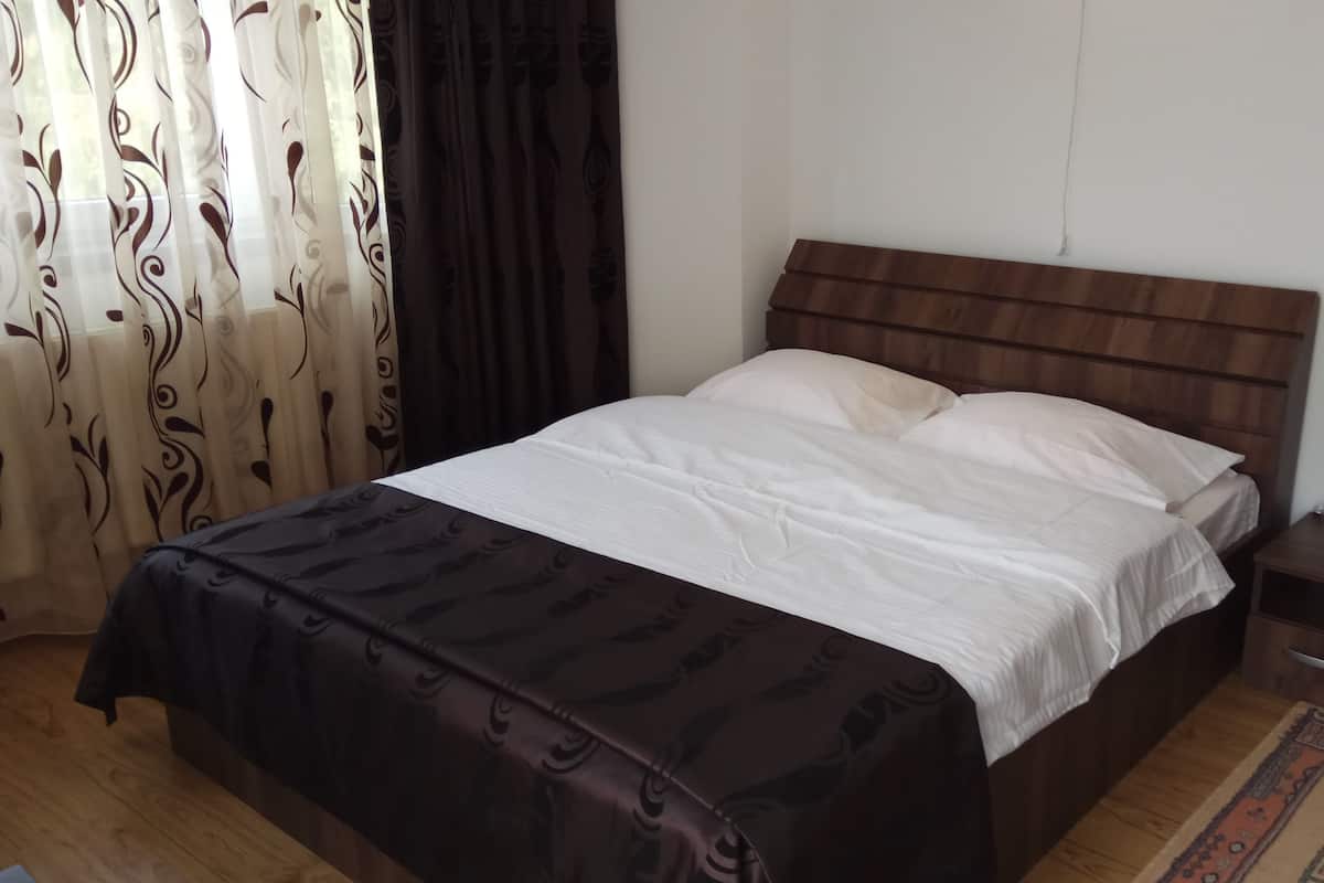 A neatly made bed with a wooden headboard, a bedside table with a lamp, and a patterned curtain.