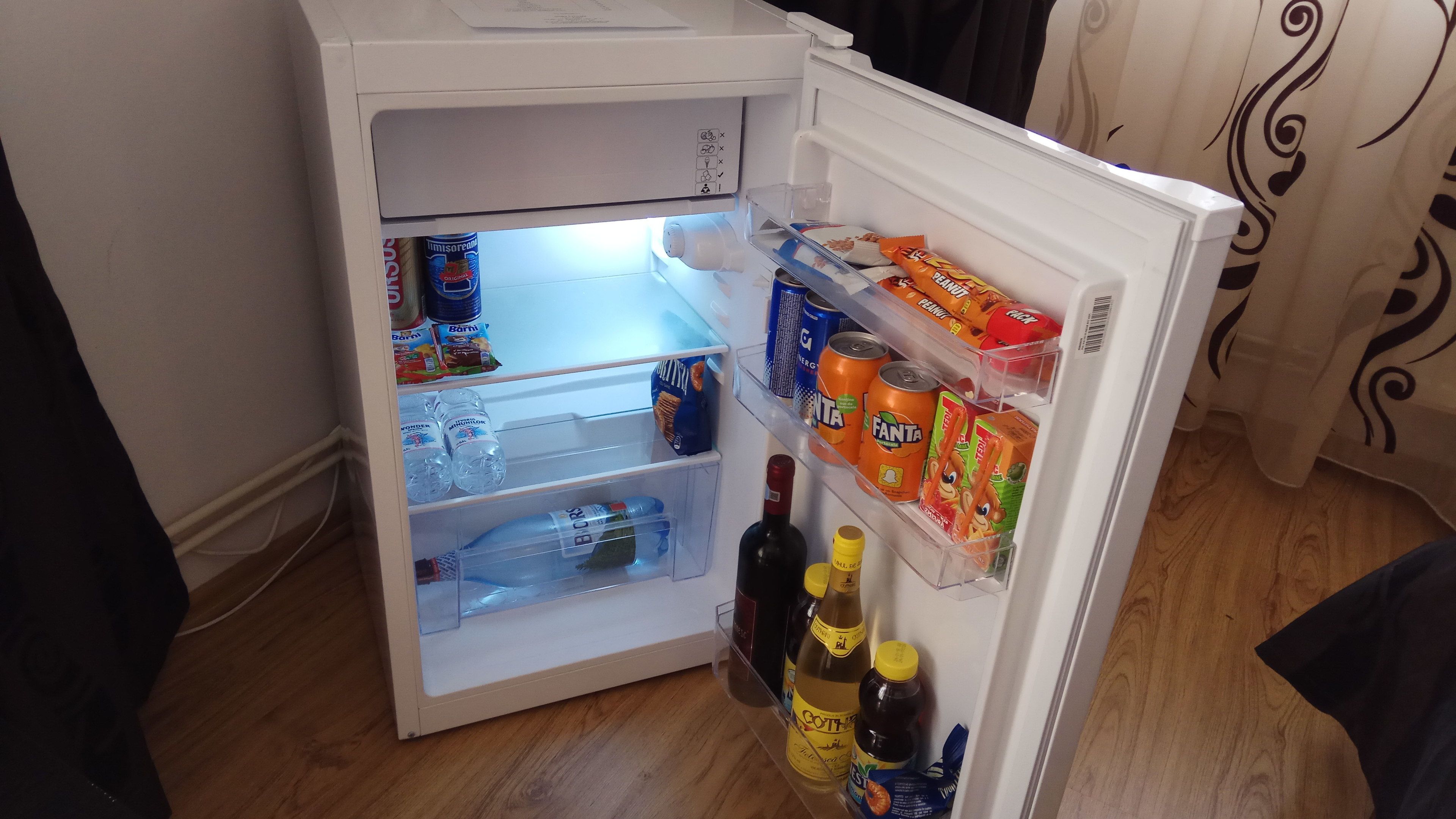Frigorifero aperto con ripiani pieni di bevande, snack e bottiglie d'acqua.