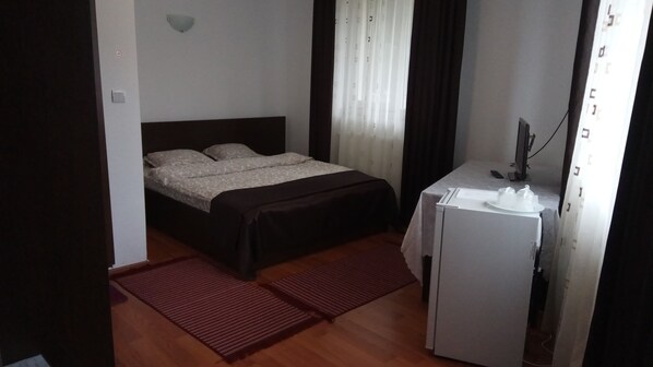 Una habitación pequeña y ordenada con cama, escritorio y refrigerador.