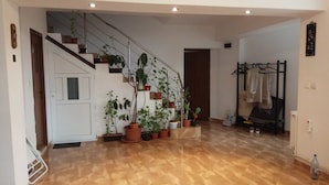 Una habitación amplia con suelo de madera, una escalera con plantas en macetas, un perchero y un radiador.