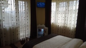 Una habitación de hotel con cama, cortinas, un televisor en la pared y una vista parcial del baño.