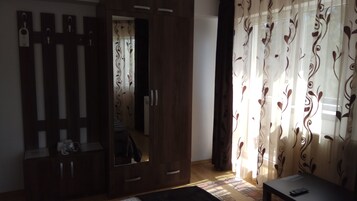 A room with a wardrobe, a bed, and a table with a remote control.