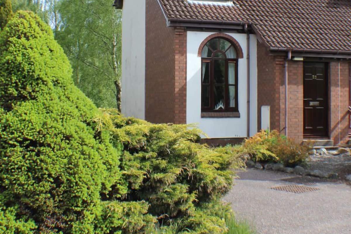 A two-story house with a brick exterior, a tiled roof, and a front entrance with a door and window.