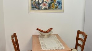 A dining table with a floral tablecloth, two wooden chairs, and a bowl on the table. A painting hangs on the wall above the table. - Eden's sweet place (Eilat)