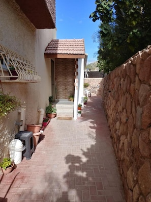 A narrow brick pathway leading to a house with a tiled roof and a stone wall on one side.