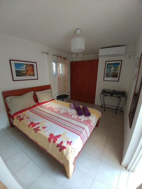 A bedroom with a bed, a wardrobe, a desk, and two paintings on the walls.