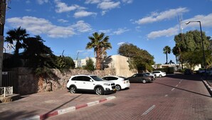 A paved street with parked cars, a stone wall, and palm trees. - Eden's sweet place (Eilat)
