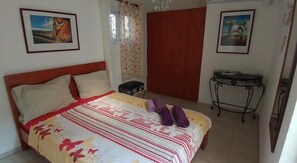A bedroom with a bed, two pillows, a bedside table, a chair, and two framed pictures on the walls.