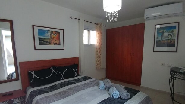 A bedroom with a large bed, a chandelier, a window with curtains, and two framed pictures on the walls. - Eden's sweet place (Eilat)