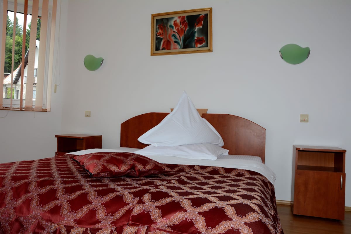 A neatly made bed with a patterned red and gold bedspread, a wooden headboard, and two bedside tables with wooden drawers.