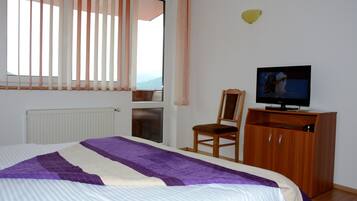 A bedroom with a bed, a television on a wooden cabinet, a chair, and a window with blinds.