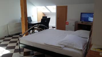 A hotel room with a bed, a desk, a chair, a radiator, a television, and a view of the sky through skylights.