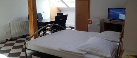 Habitación de hotel con cama, escritorio, silla, radiador, televisor y vista al cielo a través de tragaluces.