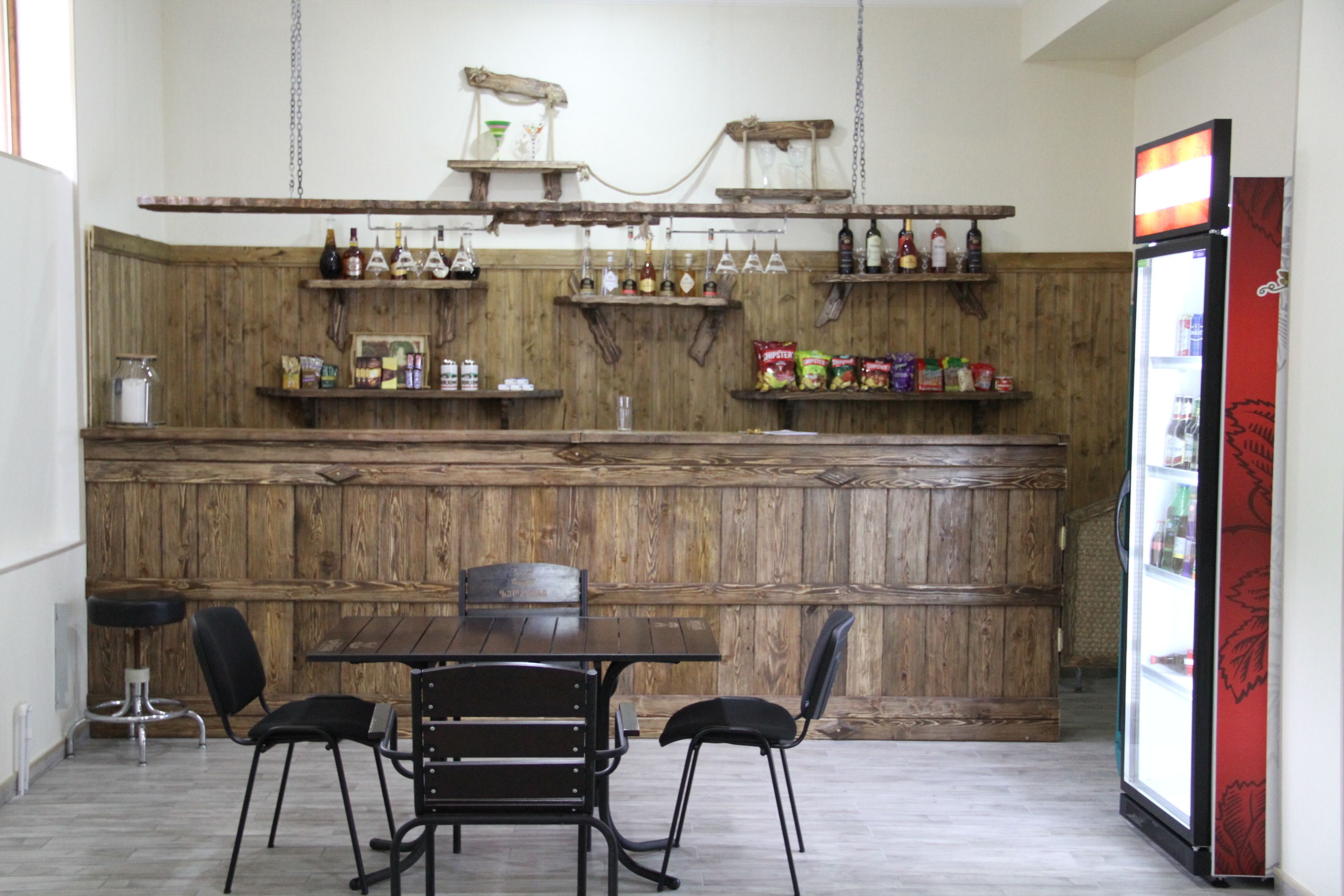 A bar area with wooden shelves, a refrigerator, and a table with chairs.