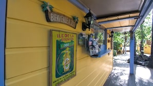 A yellow wall with a 'BIENVENUE A ZOT' sign, a 'ILE DE LA REUNION' poster, and a water dispenser. - Hotel Coco Island (Saint-Paul)