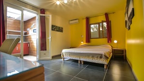 A bedroom with a bed, a chair, a desk, a window, and an air conditioning unit. - Hotel Coco Island (Saint-Paul)