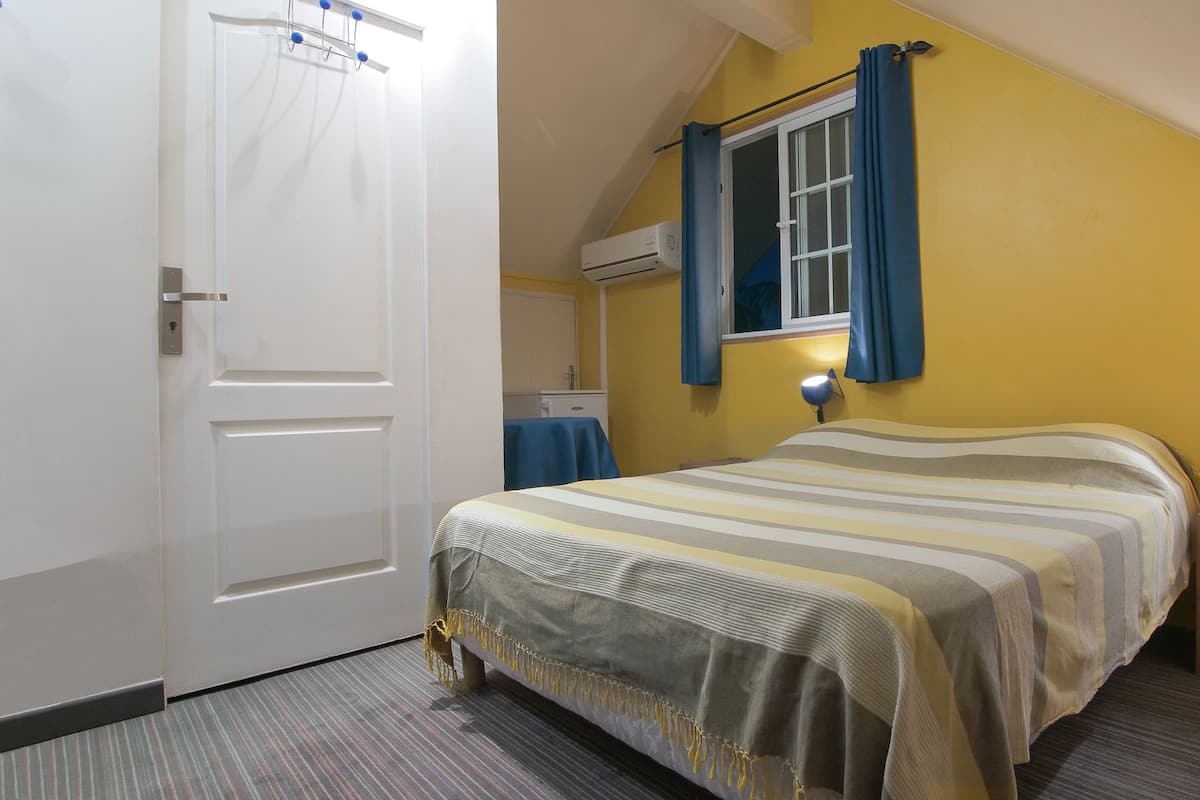 Un dormitorio con cama, mesita de noche con lámpara, ventana con cortinas y unidad de aire acondicionado.