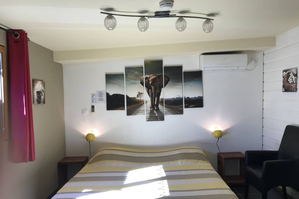 Un dormitorio con cama, dos lámparas de noche, ventilador de techo y aire acondicionado de pared.