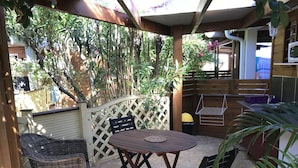 A patio with a wooden table and chairs, surrounded by a wooden fence and lush greenery. - Hotel Coco Island (Saint-Paul)