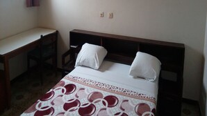 A bedroom with a bed, a desk, and a window.