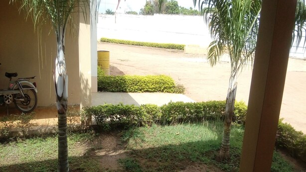 A view of a courtyard with a motorcycle parked against a wall, surrounded by greenery and a paved area.