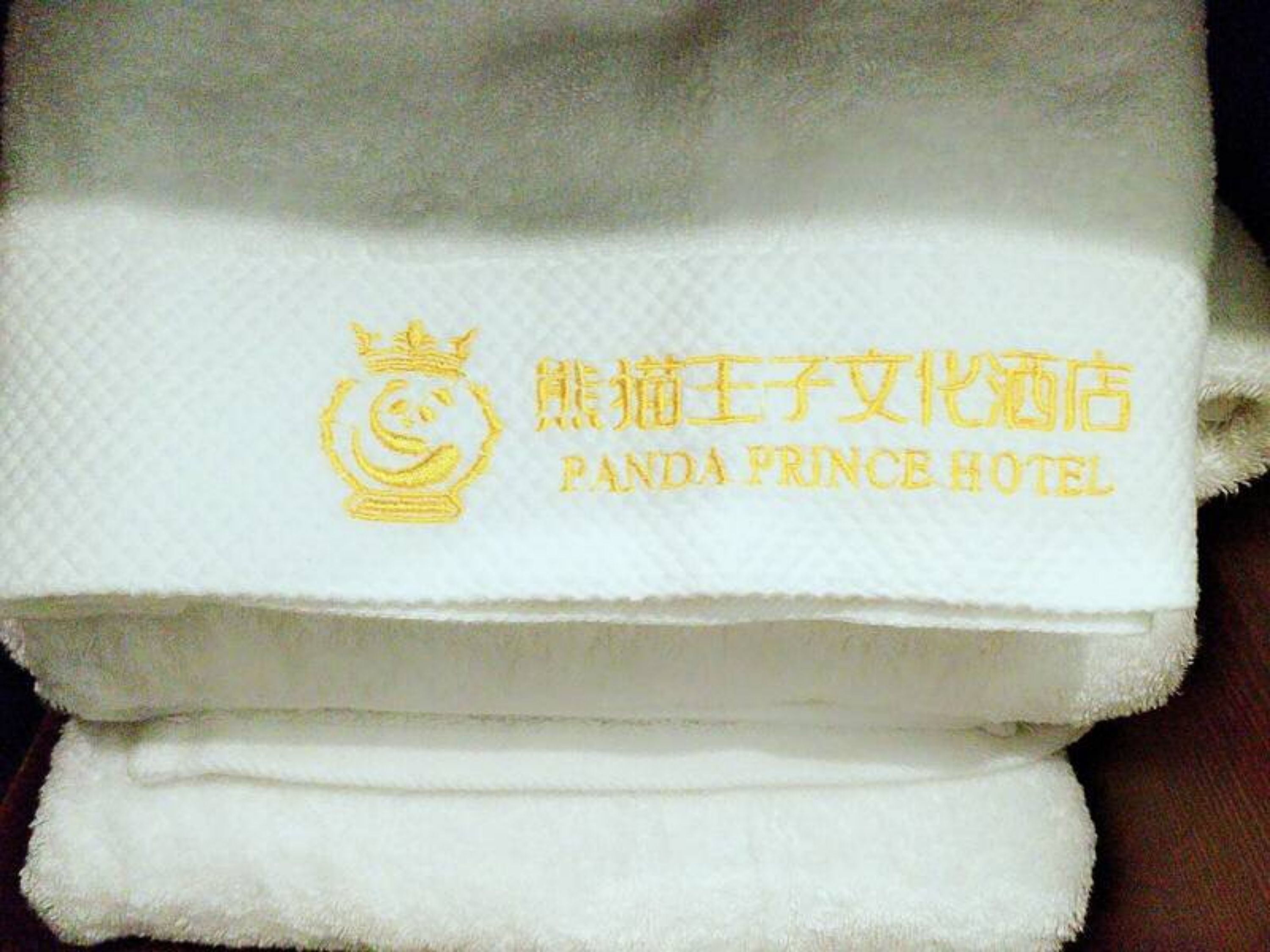 Toalla blanca doblada con el logotipo y el nombre del Hotel Panda Prince en letras doradas.
