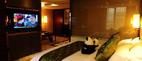 A hotel room with a bed, a television, a panda plush toy, and a large window.