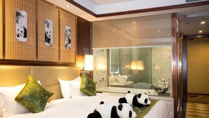 Ein Hotelzimmer mit einem großen Bett, zwei grünen Kissen, einem Kopfteil mit Panda-Motiv, einer Duschkabine aus Glas und einem Panda-Spiegelbild.