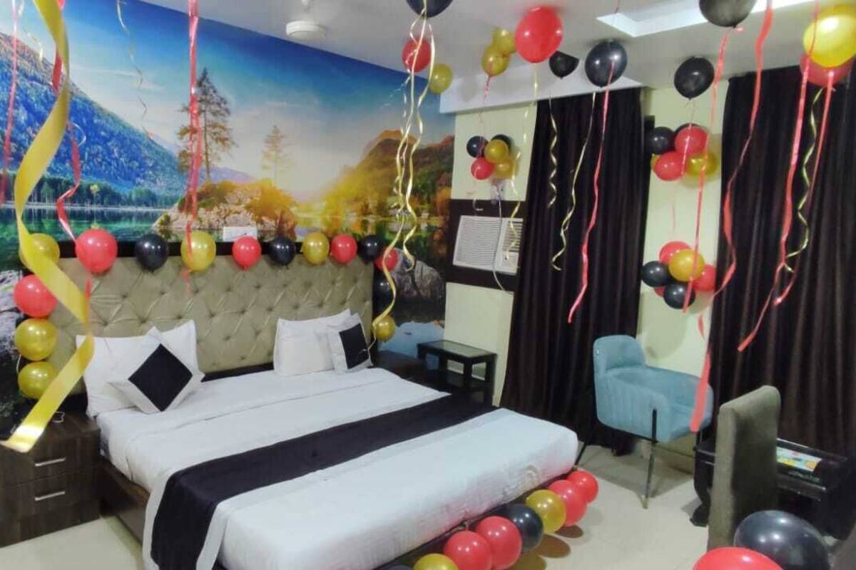 A hotel room with a large bed, a nightstand, a chair, and a desk. There are balloons and streamers decorating the room.