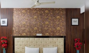Habitación de hotel con cabecera capitonada, papel tapiz floral y paneles de madera.
