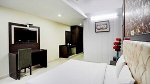 Une chambre d’hôtel avec un lit, un bureau, une télévision, une armoire et un tableau au mur.