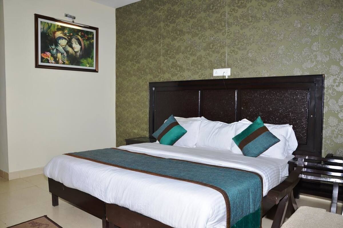 A hotel room with a large bed, a nightstand, a framed picture on the wall, and a patterned wallpaper.