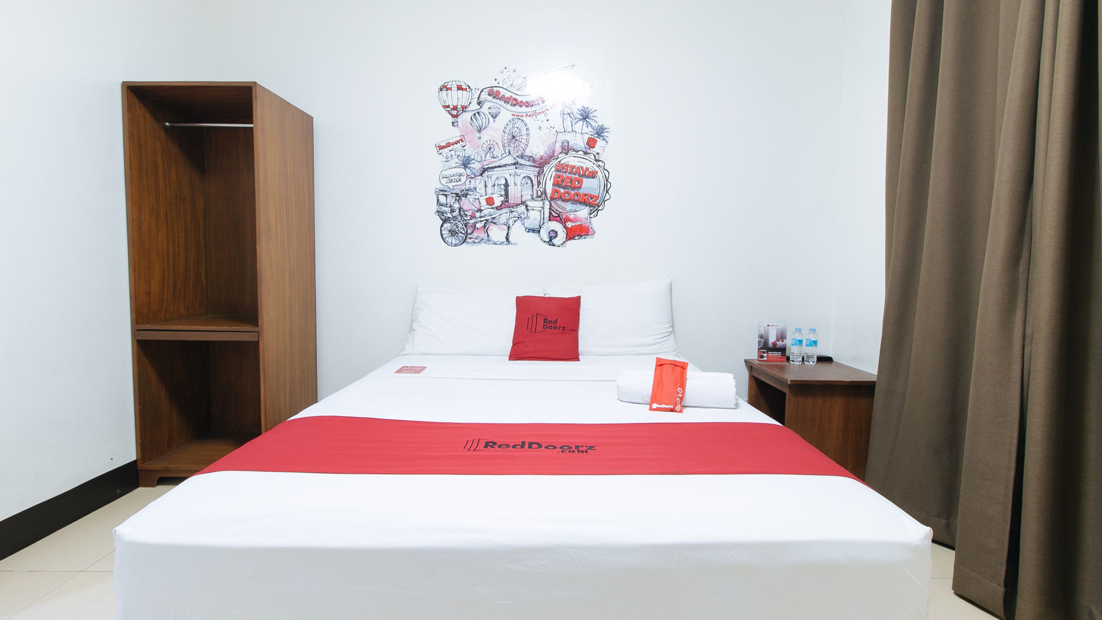 Una habitación de hotel con una cama, un armario de madera, una mesita de noche con botellas de agua y un mural en la pared.