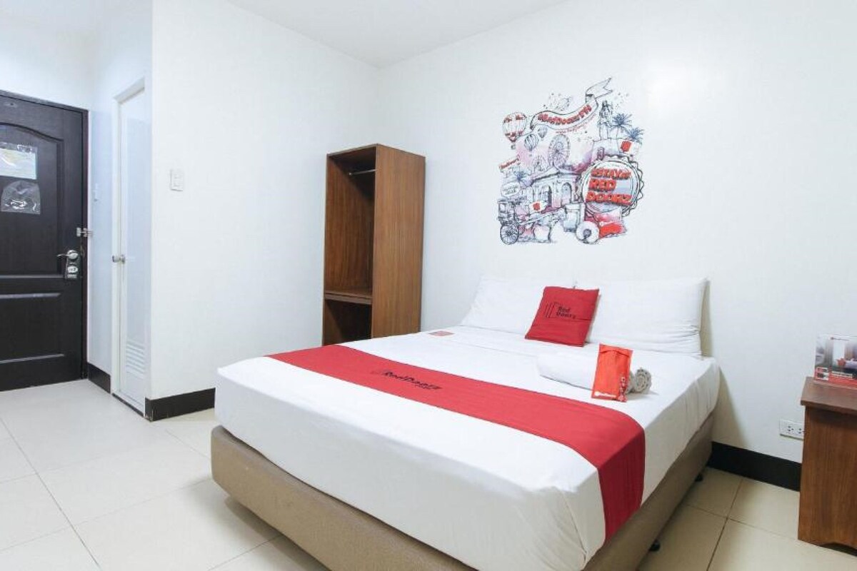 Una habitación de hotel con cama, armario de madera, decoración en la pared y una mesita con botellas de agua.