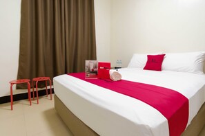 A hotel room with a bed, a red bedspread, a red pillow, a red stool, and a water bottle. - RedDoorz Plus @ EDSA Congressional (Quezon City)