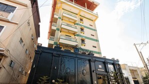 Un edificio de varios pisos con balcones, un portón negro y plantas decorativas.