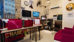 Un hall de hotel con un sofá rojo, una exhibición de equipaje Chanel, un letrero RedDoor, un televisor y una tocador con espejo.